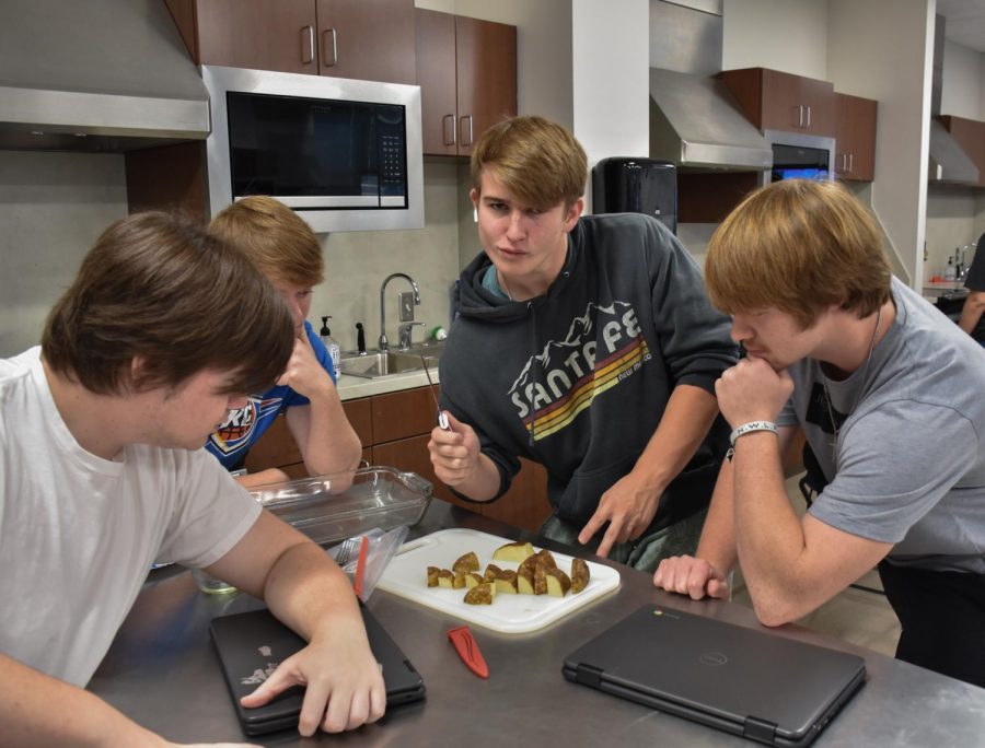 Parker Veader (12), Luke Howard (12), and Jacob Howard (12) are watching as Andrew Escalante (12) is about to cut the potatoes thinner.